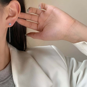 Close-up of minimalist silver drop earrings with light blue gem and long tassel chain