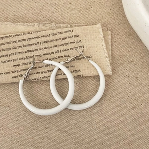 Détail de boucles d'oreilles créoles blanches en résine sur tissu vintage épuré