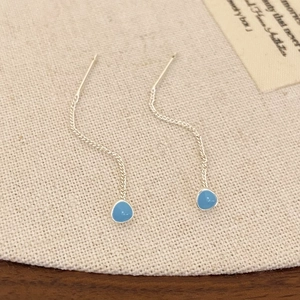 Detailed view of silver chain earrings with light blue teardrop pendants on fabric
