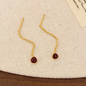 Detail view of red teardrop tassel earrings with wavy gold chain on burlap background