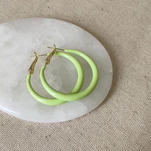 Détail de boucles d'oreilles rondes vert clair mat sur plateau marbre et tiges dorées