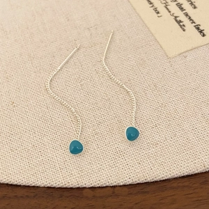 Macro view of silver tassel earrings with teal enamel drops on beige linen fabric