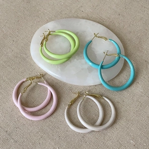 Détail de créoles mates colorées en vert, bleu, rose et blanc sur tissu en lin