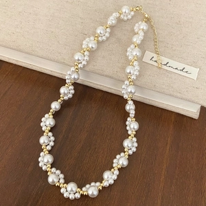 Elegant handmade white pearl necklace with gold beads and lobster clasp on wooden background