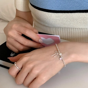 Detail of silver bow bracelet with pearl and pink heart charm set with floral ring