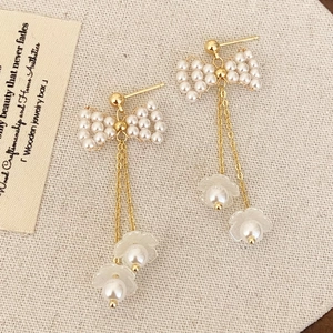 Elegant gold bow pearl tassel earrings with floral charms on a textured background