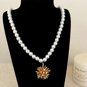 Elegante collana di perle con ciondolo a fiore dorato su espositore nero