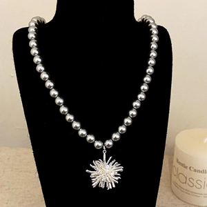 Elegante collana di perle grigie con ciondolo a stella d'argento su un supporto nero