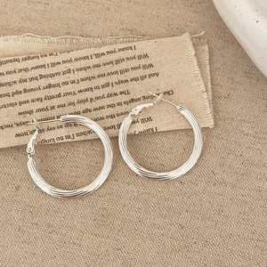 Minimalist silver triple-line hoop earrings with vintage linen background and soft lighting