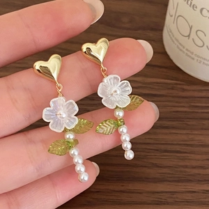 Élégantes boucles d'oreilles cœur dorées avec fleur blanche et perles sur fond bois