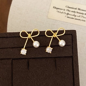 Elegant gold bow earrings with freshwater pearls and zircon stones on a display board
