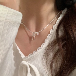 Close-up of bow and pearl pendant necklace worn by a model against lace fabric