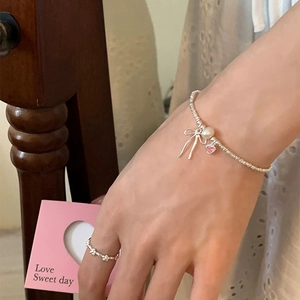 Detail of silver bow necklace with pearl and pink heart gemstone on hand