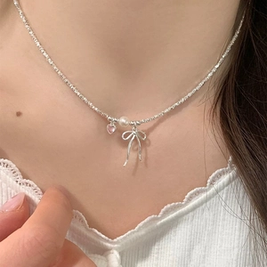 Detail of a thin shimmering chain necklace with a silver bow, pearl, and pink heart pendant