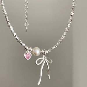 Detail of silver bow necklace with pink heart gem and white pearl pendant close-up