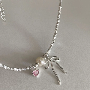 Close-up of pearl necklace with silver bow and pink heart zircon pendant detail