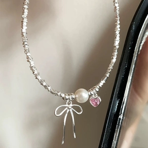 Macro detail of silver bow pendant with pink heart gemstone and round pearl necklace