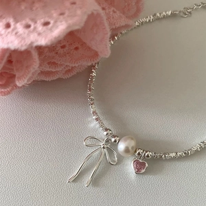 Detail view of a silver bow necklace with a white pearl and a pink heart zircon pendant