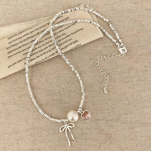 Detail of beaded necklace with pearl, pink heart, and silver bow charm on vintage paper