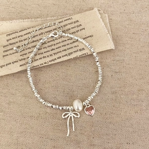 Detail of silver beaded bracelet with pearl, pink heart charm and bow on linen fabric