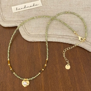 Détail du collier de perles vertes fait main avec pendentif cœur sur fond de lin vintage