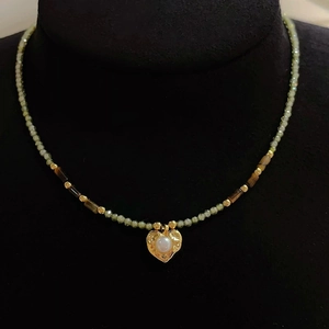 Détail du collier de perles vertes avec pendentif cœur doré orné d'une perle centrale