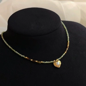 Détail d'un collier de perles vintage avec perles vertes et pendentif cœur doré et perle