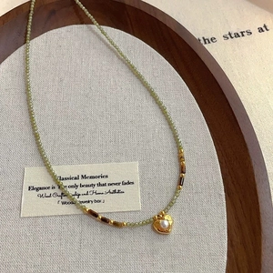 Détail du collier de perles facettées vert clair avec pendentif cœur perlé doré