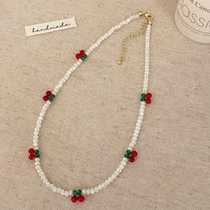 Collier artisanal perlé de cristaux blancs avec breloques cerise sur tissu beige