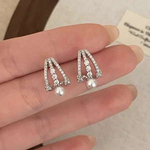 Micro-pave zircon triangle stud earrings with hanging white pearls on a textured background