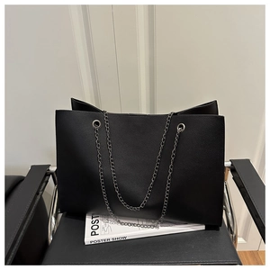 Dettaglio borsa tote in pelle nera con catene argentate su una sedia di design