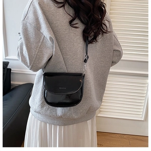 Detail of glossy black patent leather saddle bag with adjustable shoulder strap