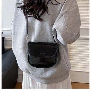 Close-up of a black glossy patent leather crossbody bag with letter embossed detail