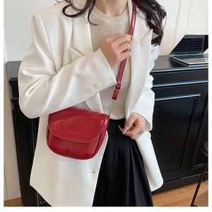 Close-up of red saddle crossbody bag in glossy faux leather with silver hardware