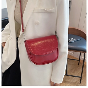 Detail of dark red glossy saddle bag with embossed fashion text and slim shoulder strap