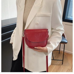 Macro shot of red glossy patent leather saddle bag featuring silver metal hardware details