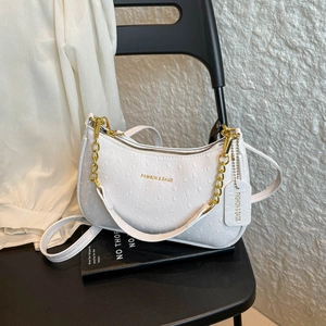 Borsa sottobraccio bianca con trama struzzo e catena dorata su sedia moderna nera