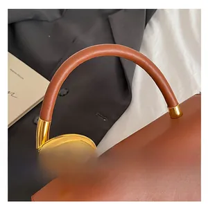 Detail of caramel leather saddle bag handle with golden twisted metal hardware link