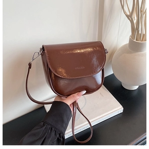 Detail of dark brown glossy leather crossbody bag with flap and silver hardware