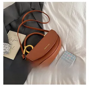 Detail of a brown saddle bag with golden ring handle and logo on white fabric