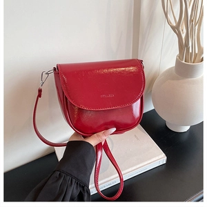 Detail of burgundy glossy leather saddle bag with NYLLZZA embossing and crossbody strap
