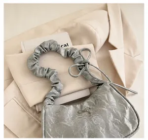 Detail of grey pleated crescent shoulder bag featuring silver metal bow and soft handle