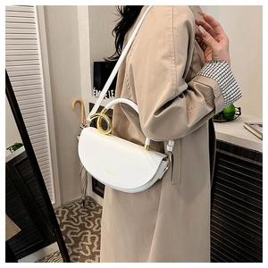 Detail of white saddle bag featuring large gold ring handle and leather texture