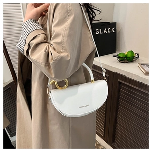 Close-up of white crescent saddle bag with gold metal circular handle on beige trench coat