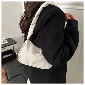 Detail of off-white crescent underarm bag featuring a delicate black bow and ruched strap