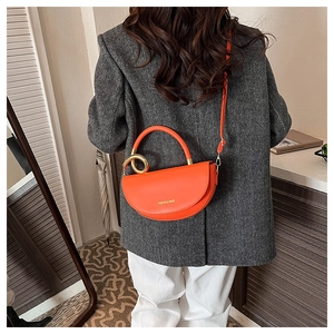 Detail of a bright orange leather saddle bag with a large gold metal ring and slim strap