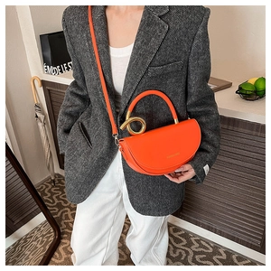 Detail of bright orange saddle bag with gold metal handle and shoulder strap worn by model