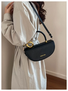 Black leather crescent saddle bag with gold ring handle worn as a crossbody style