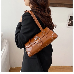 Brown patent leather shoulder bag with silver studs and buckles on a female model