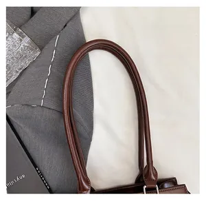 Close-up of the smooth dark brown leather top handle with silver metal rings on a square bag